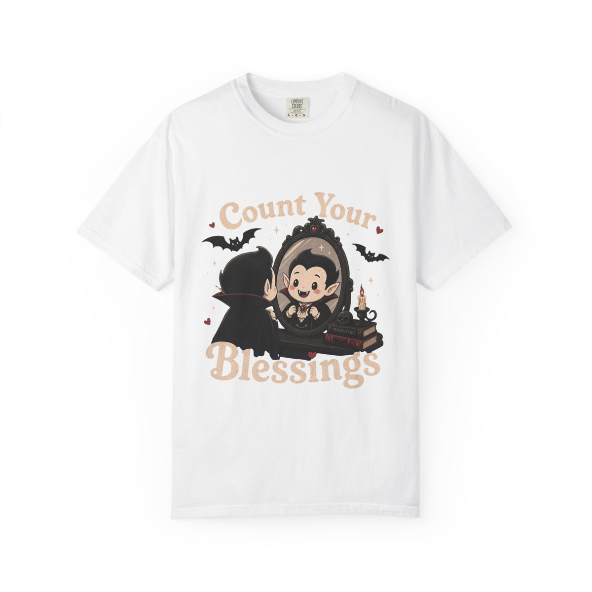 A white short-sleeve crewneck t-shirt featuring a cute cartoon graphic of a vampire smiling at mirror, with the text 'Count Your Blessings' in a peach-colored font.
