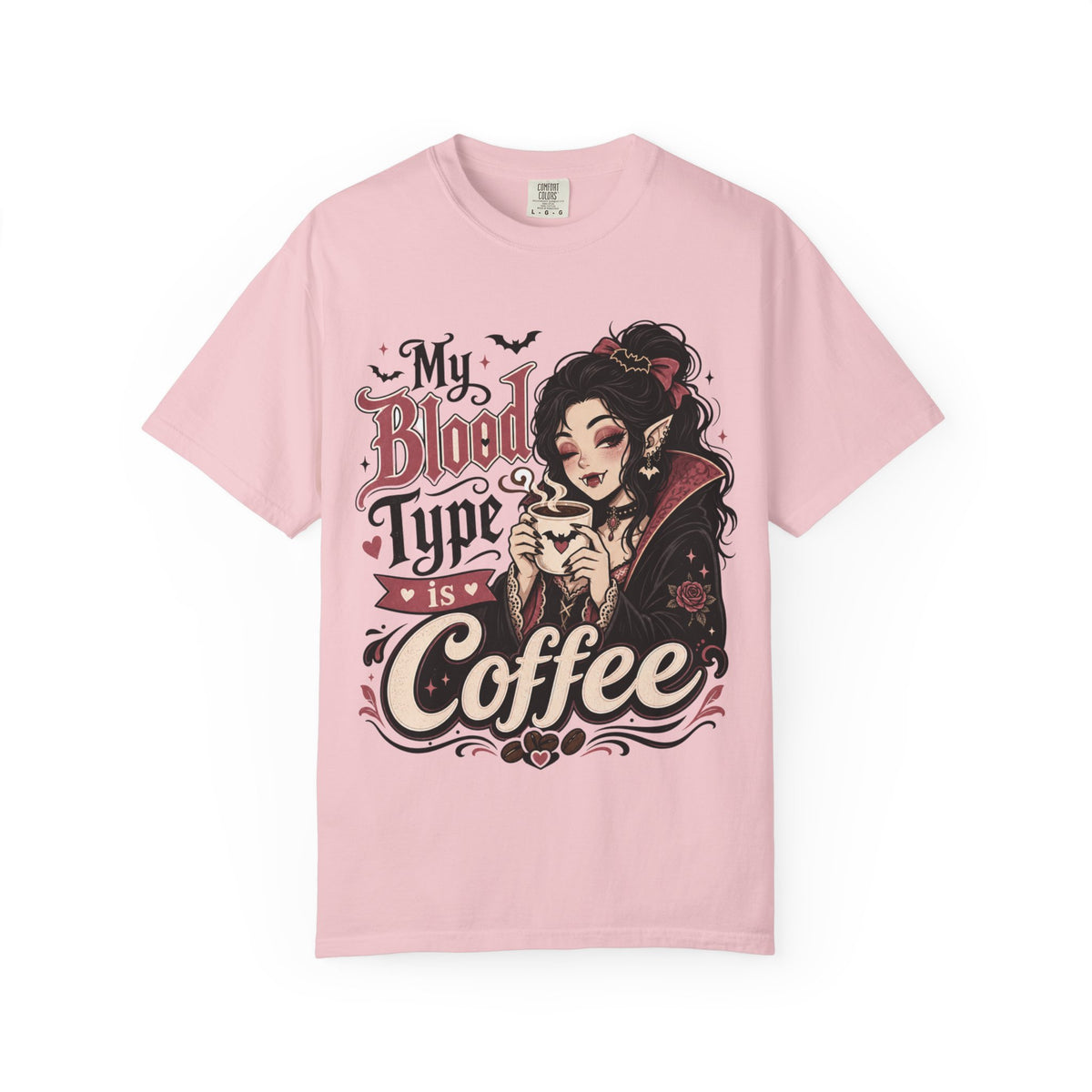 A light pink short-sleeve crewneck t-shirt featuring a gothic-style graphic print of a vampire woman and the text 'My Blood Type is Coffee' in stylized red and beige lettering.