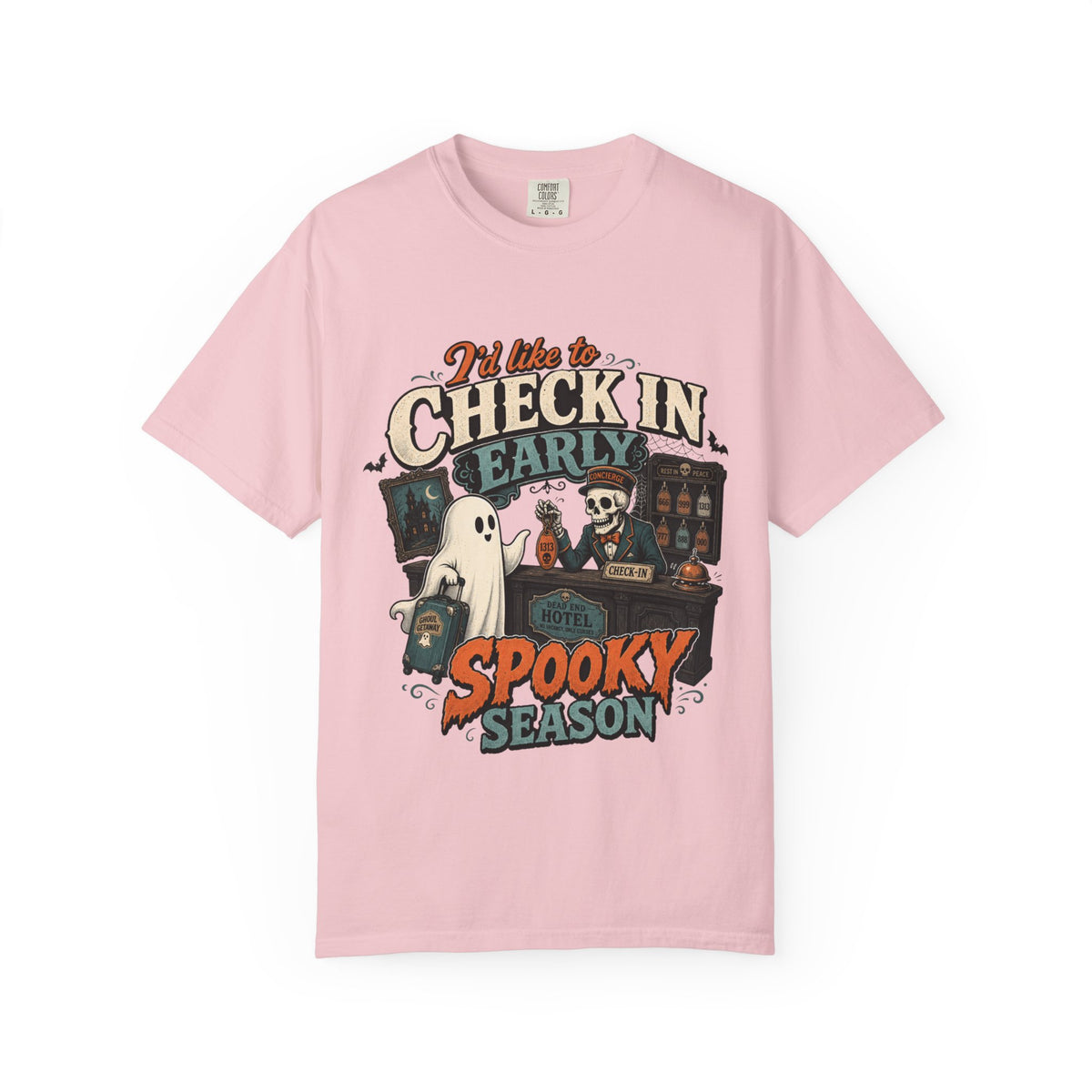 A pink short-sleeve crewneck t-shirt featuring a colorful graphic print on the front with the text 'I'd like to CHECK IN EARLY SPOOKY SEASON' and illustrations of a skeleton concierge, a ghost, and a haunted house.