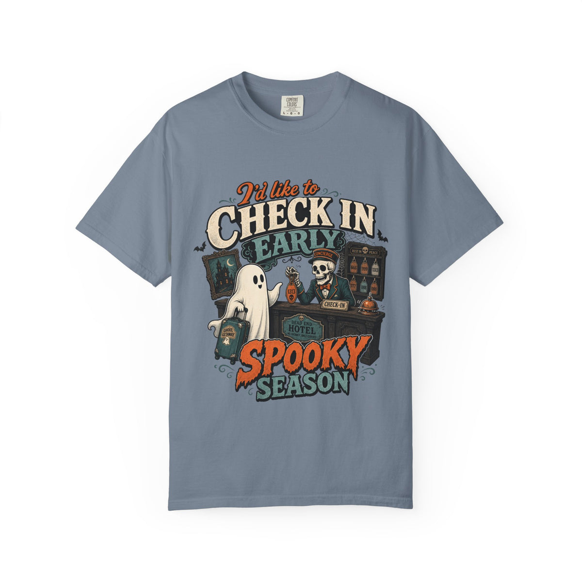 A slate blue short-sleeve crewneck t-shirt featuring a colorful graphic print on the front with the text 'I'd like to CHECK IN EARLY SPOOKY SEASON' and illustrations of a skeleton concierge, a ghost, and a haunted house.