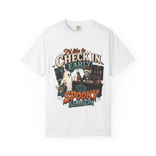 A white short-sleeve crewneck t-shirt featuring a colorful graphic print on the front with the text 'I'd like to CHECK IN EARLY SPOOKY SEASON' and illustrations of a skeleton concierge, a ghost, and a haunted house.