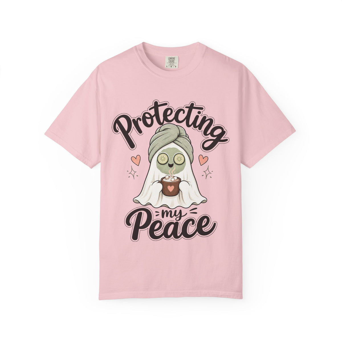 A light pink short-sleeve crewneck t-shirt featuring a graphic of a cartoon ghost wearing a green head wrap, spa mask and holding a cup, with the text 'Protecting my Peace' written in black script.