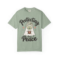 A sage green short-sleeve crewneck t-shirt featuring a graphic of a cartoon ghost wearing a green head wrap, spa mask and holding a cup, with the text 'Protecting my Peace' written in black script.