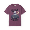 A dark purple short-sleeve crewneck t-shirt featuring a cute Halloween graphic of a ghost reading a book on top of a tombstone that says 'RIP', with the words 'Read In Peace' written in stylized lettering.