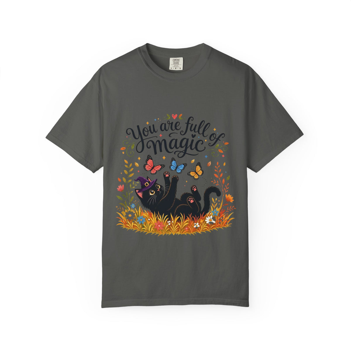 A dark gray short-sleeve crewneck t-shirt featuring a colorful graphic print on the front. The design includes the text 'You are full of magic' in a black script font, above an illustration of a black cat surrounded by colorful butterflies, flowers, and grass.