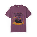 A dark purple short-sleeve crewneck t-shirt featuring a colorful graphic print on the front. The design includes the text 'You are full of magic' in a black script font, above an illustration of a black cat surrounded by colorful butterflies, flowers, and grass.