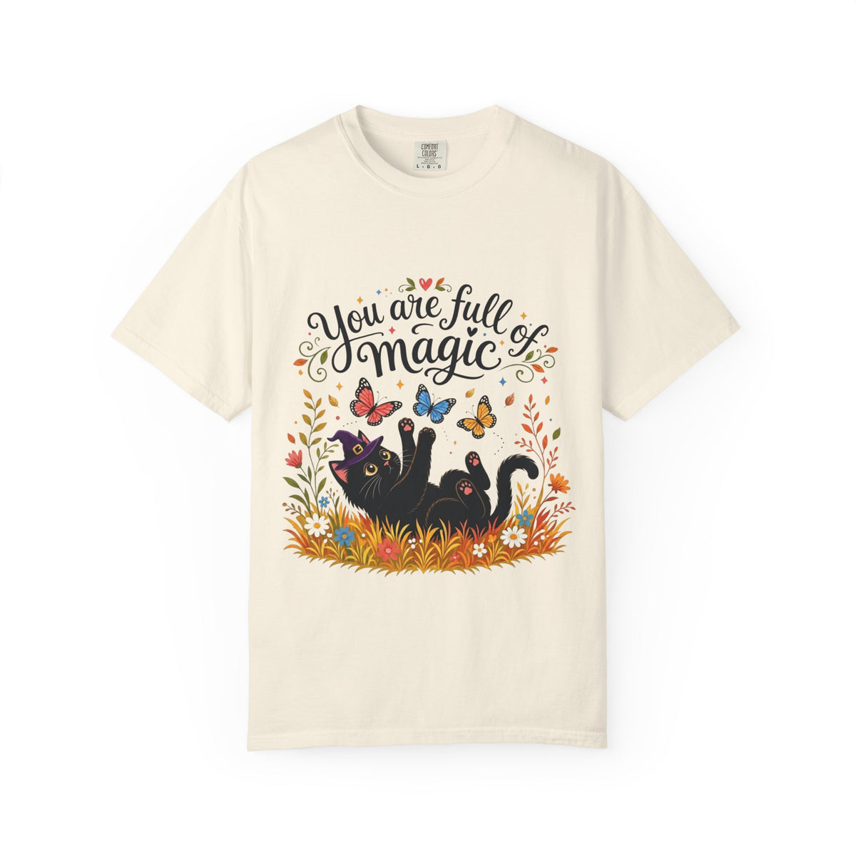 An off-white short-sleeve crewneck t-shirt featuring a colorful graphic print on the front. The design includes the text 'You are full of magic' in a black script font, above an illustration of a black cat surrounded by colorful butterflies, flowers, and grass.
