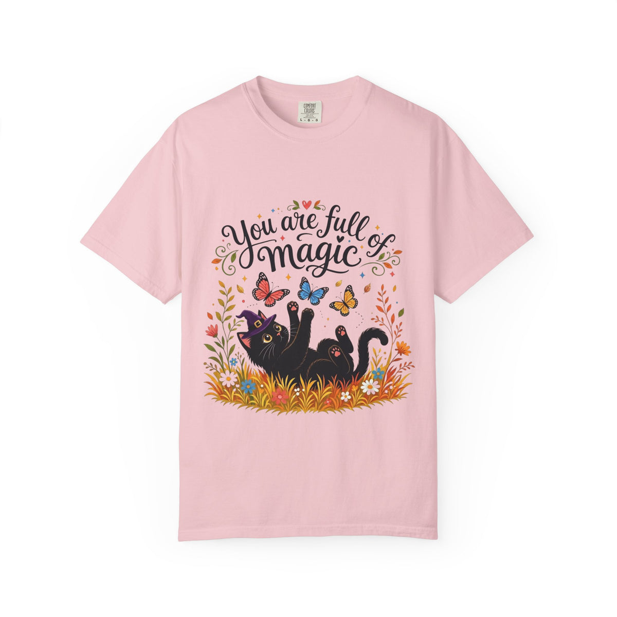 A pink short-sleeve crewneck t-shirt featuring a colorful graphic print on the front. The design includes the text 'You are full of magic' in a black script font, above an illustration of a black cat surrounded by colorful butterflies, flowers, and grass.