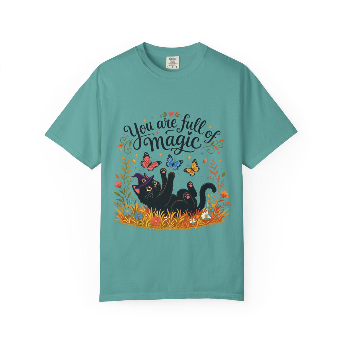A teal short-sleeve crewneck t-shirt featuring a colorful graphic print on the front. The design includes the text 'You are full of magic' in a black script font, above an illustration of a black cat surrounded by colorful butterflies, flowers, and grass.