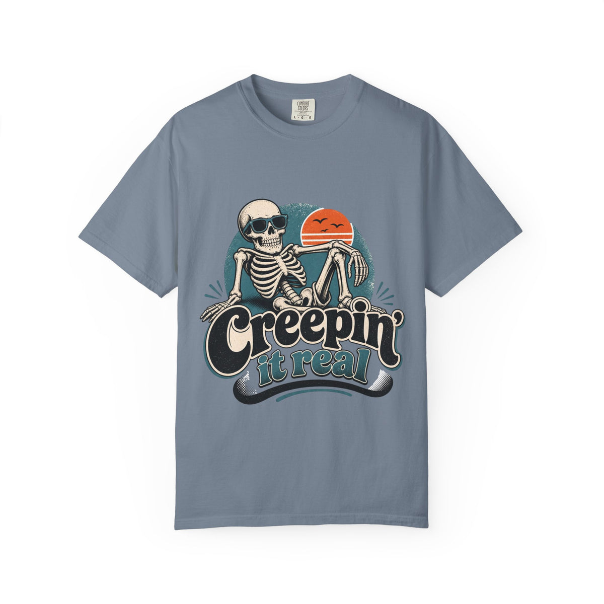 A blue short-sleeve crewneck t-shirt featuring a retro graphic of a skeleton sitting next to an orange sun, with the text 'Creepin' it real' printed below.