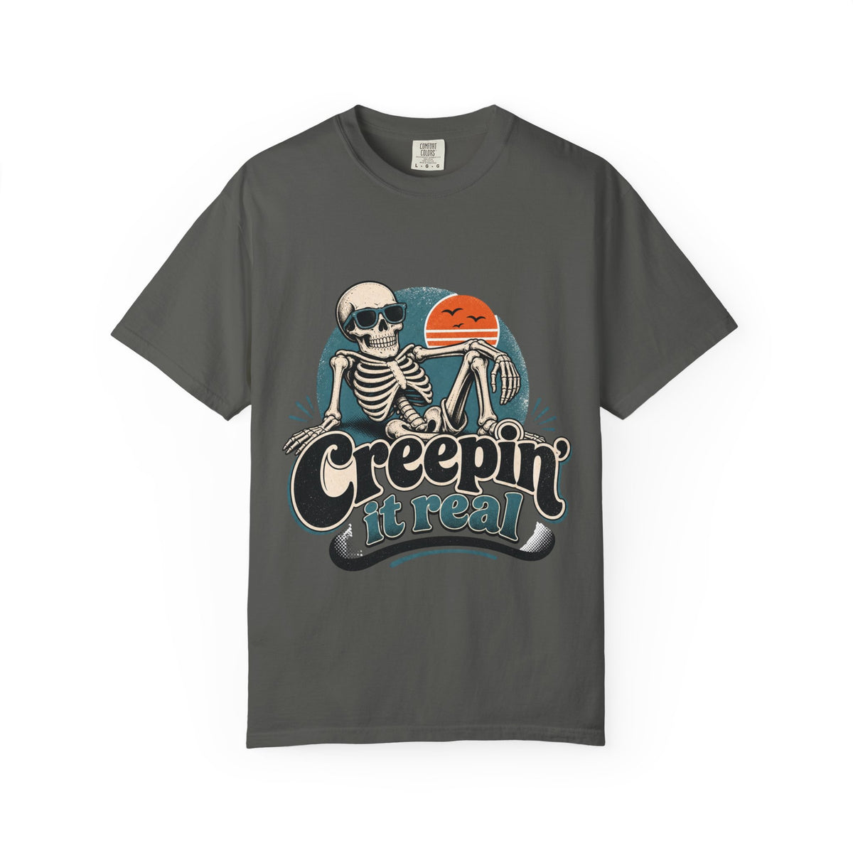 A dark gray short-sleeve crewneck t-shirt featuring a retro graphic of a skeleton sitting next to an orange sun, with the text 'Creepin' it real' printed below.