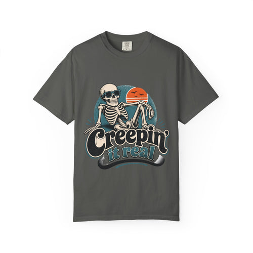 A dark gray short-sleeve crewneck t-shirt featuring a retro graphic of a skeleton sitting next to an orange sun, with the text 'Creepin' it real' printed below.