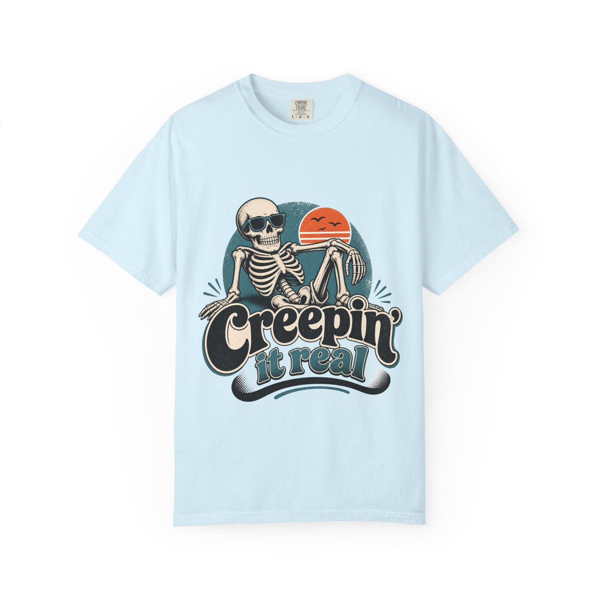 A ice blue short-sleeve crewneck t-shirt featuring a retro graphic of a skeleton sitting next to an orange sun, with the text 'Creepin' it real' printed below.
