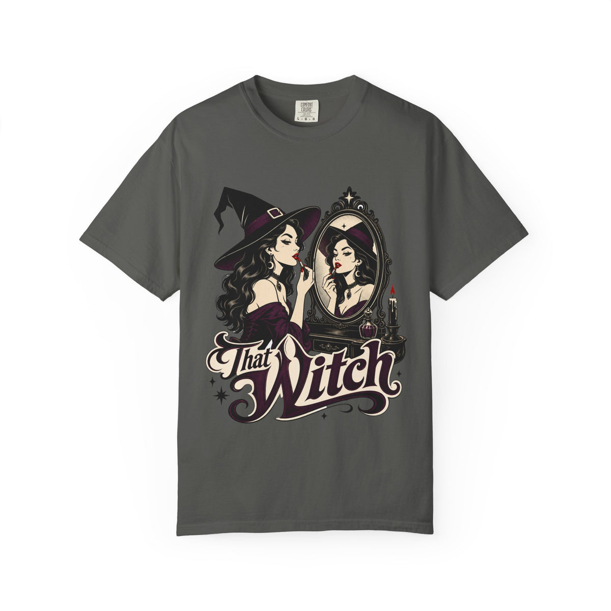 A dark gray short-sleeve crewneck t-shirt featuring a graphic print of a witch applying lipstick in front of a mirror, with the text 'That Witch' written below in a stylized font.