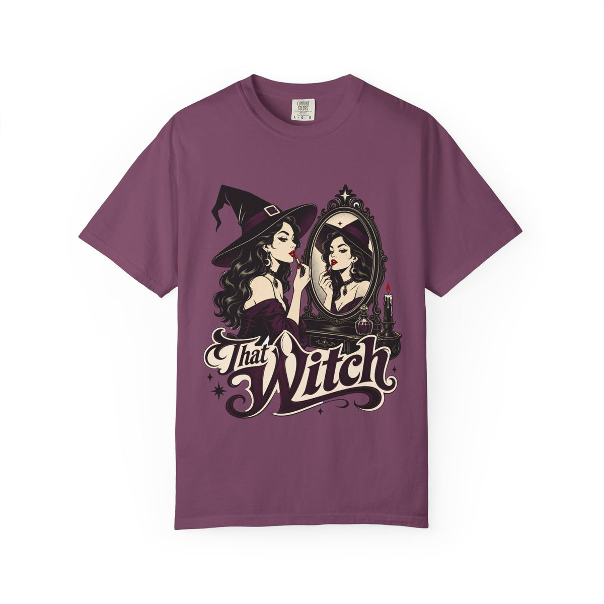 A dark purple short-sleeve crewneck t-shirt featuring a graphic print of a witch applying lipstick in front of a mirror, with the text 'That Witch' written below in a stylized font.