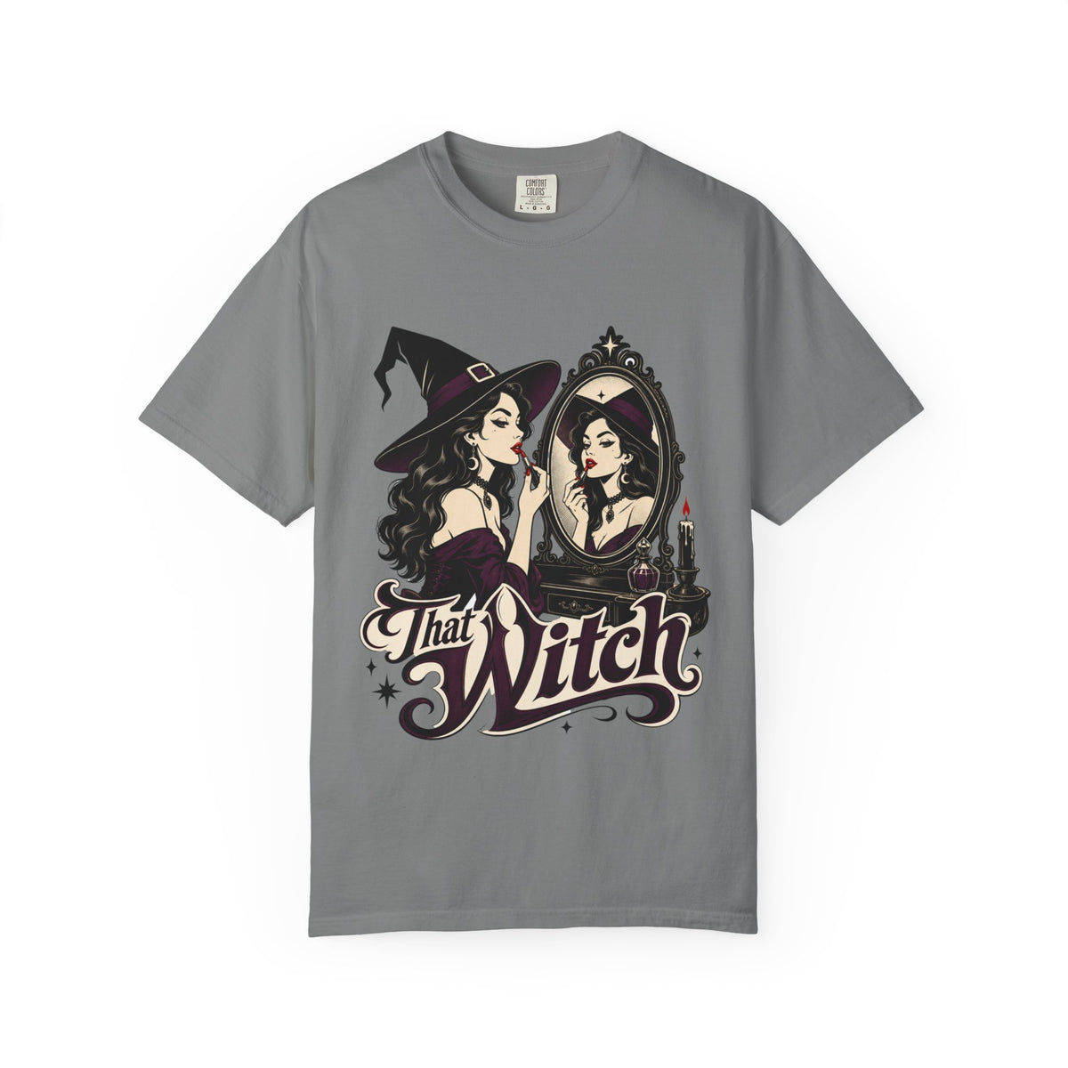 A gray short-sleeve crewneck t-shirt featuring a graphic print of a witch applying lipstick in front of a mirror, with the text 'That Witch' written below in a stylized font.