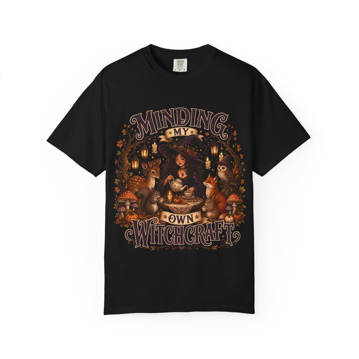 A black short-sleeve crewneck t-shirt featuring a large, detailed graphic that depicts a witch surrounded by autumn elements like foxes, a cat, pumpkins, and lanterns, with the text 'MINDING MY OWN WITCHCRAFT' in a stylized font.
