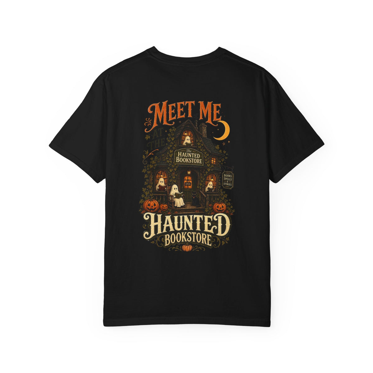 A black short-sleeve t-shirt with a detailed graphic on the front depicting a haunted bookstore at night, complete with pumpkins, a ghost, and orange text reading 'MEET ME AT THE HAUNTED BOOKSTORE'.