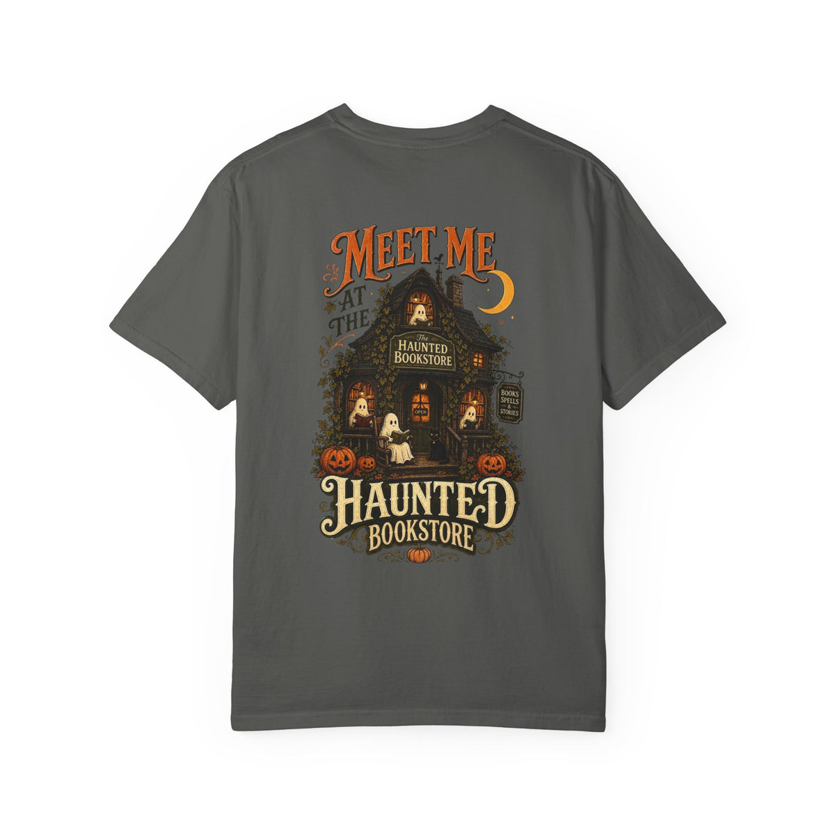 A dark gray short-sleeve t-shirt with a detailed graphic on the front depicting a haunted bookstore at night, complete with pumpkins, a ghost, and orange text reading 'MEET ME AT THE HAUNTED BOOKSTORE'.