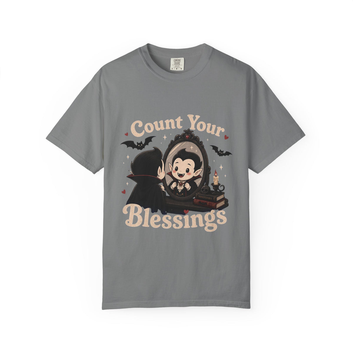A gray short-sleeve crewneck t-shirt featuring a cute cartoon graphic of a vampire smiling at mirror, with the text 'Count Your Blessings' in a peach-colored font.