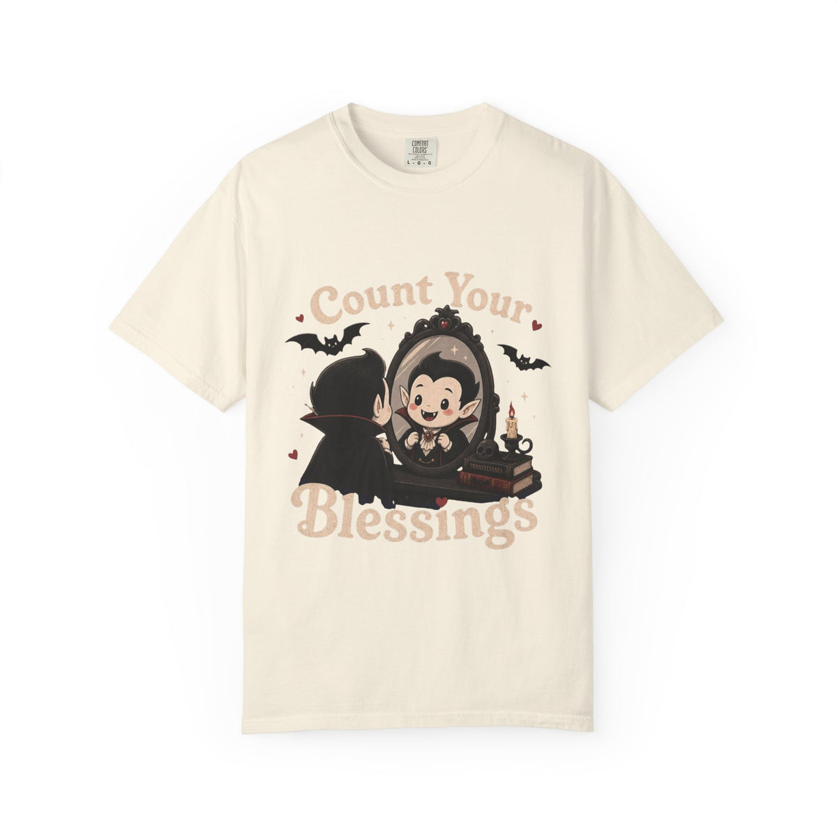 A off-white short-sleeve crewneck t-shirt featuring a cute cartoon graphic of a vampire smiling at mirror, with the text 'Count Your Blessings' in a peach-colored font.