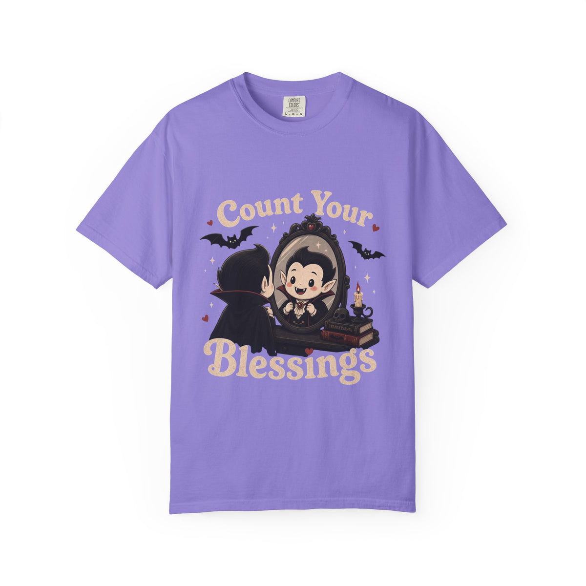 A purple short-sleeve crewneck t-shirt featuring a cute cartoon graphic of a vampire smiling at mirror, with the text 'Count Your Blessings' in a peach-colored font.
