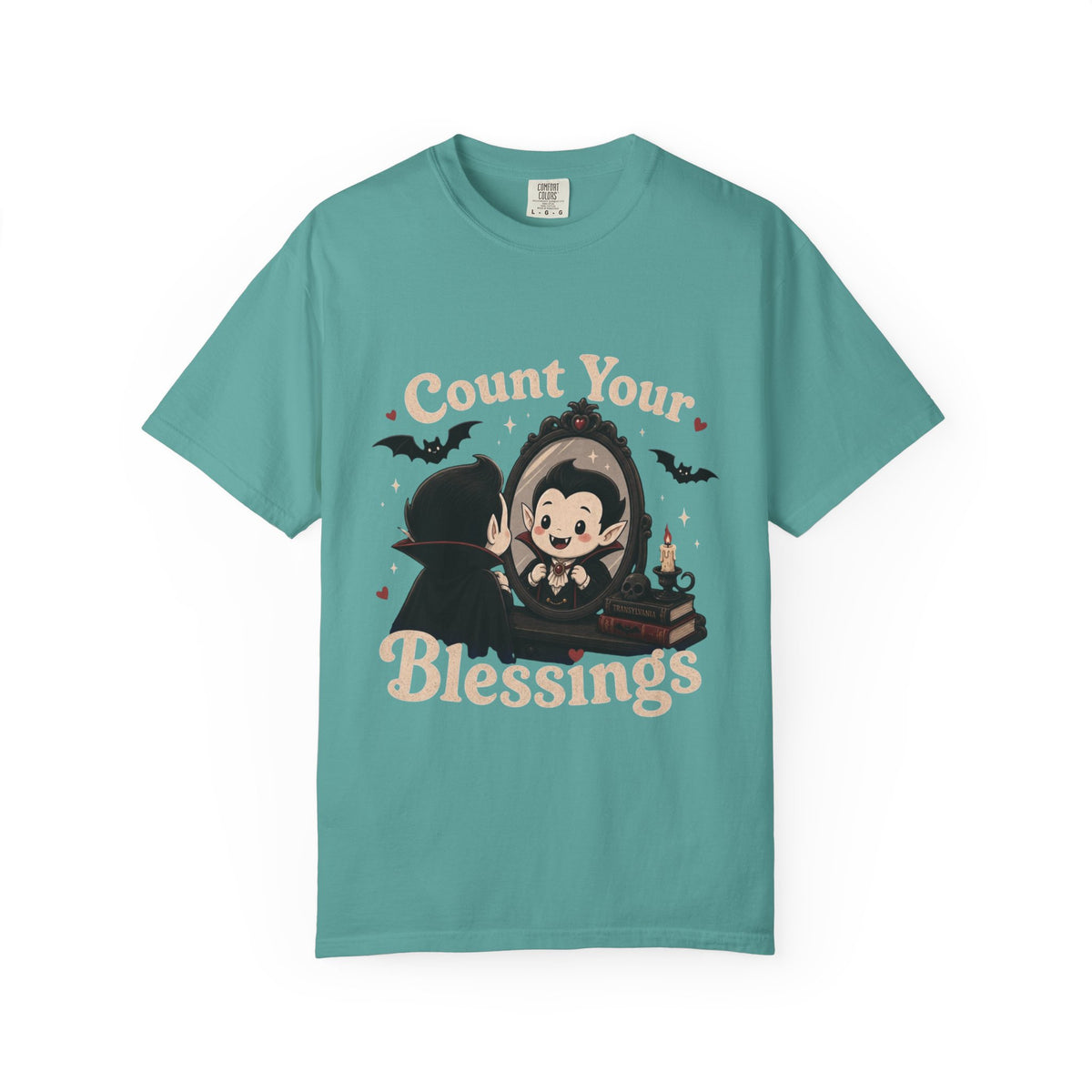 A teal short-sleeve crewneck t-shirt featuring a cute cartoon graphic of a vampire smiling at mirror, with the text 'Count Your Blessings' in a peach-colored font.