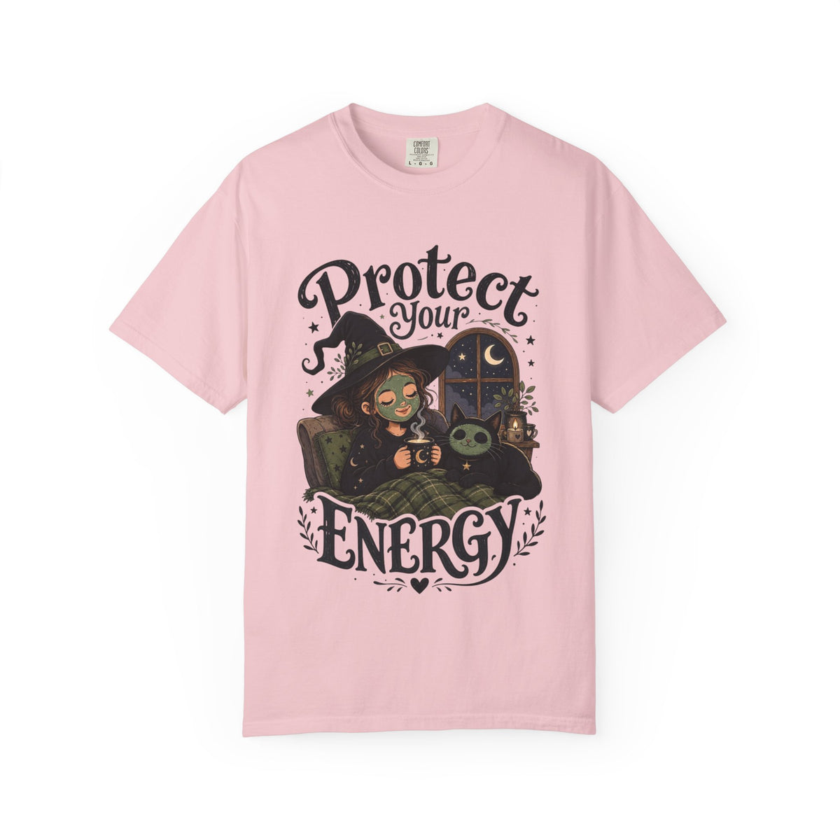 A pink short-sleeve crewneck t-shirt featuring a graphic showing a cartoon witch sitting in bed with her cat, both wearing spa face masks, under a window with crescent moon, with the text 'Protect Your Energy' written in a gothic font.